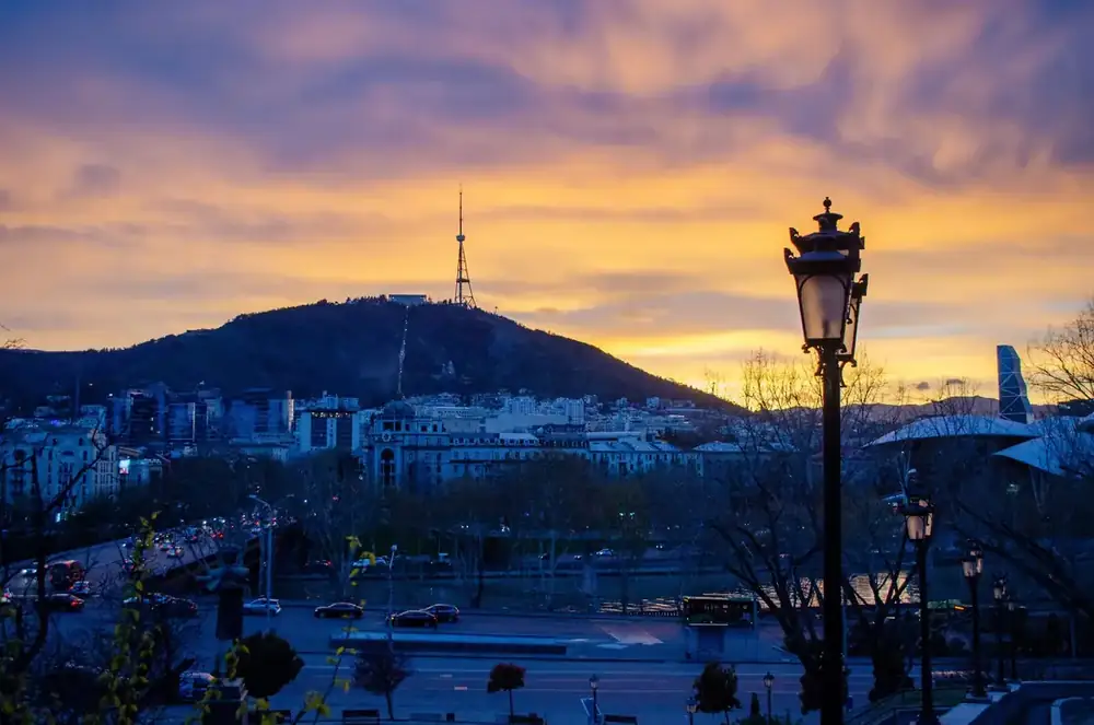 Tbilisi rooftops and the Mtatsminda tower against a soft sunset sky